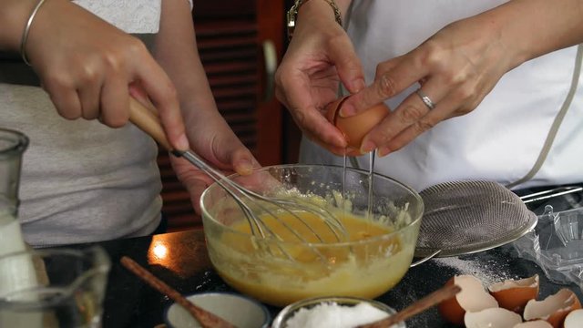 Close-up view of female hands breaking egg, pouring yolk from one half of shell to another and whisking it in bowl with flour on kitchen table