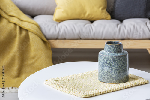 Close-up on grey vase on pad on round table in modern living room interior with yellow. Real photo
