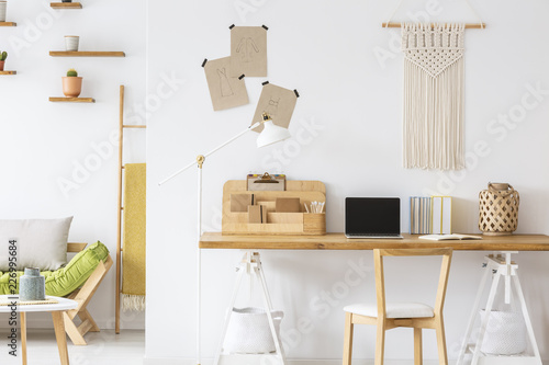 Wooden chair at desk with laptop and organizer in white home office interior with decor. Real photo