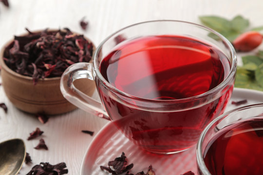 Hot red karkade tea in glass cups with dry tea on a white wooden table