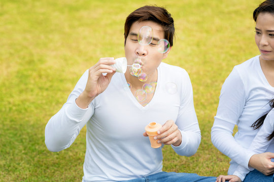 Happy young father and her daughter blowing soap bubbles togeter in park.Family happiness and carefree concept.