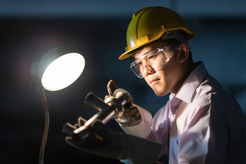 Mechanic Engineer Turner Miller verifies the accuracy of manufacturing steel parts with a scale the size of the measurement device. In the dark room with lamp background. © Nattanon