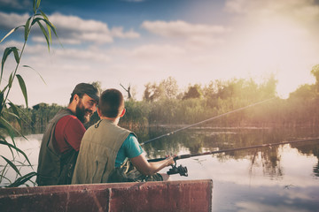 father and son sitting in boat on lake while fishing together