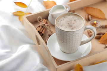 Autumn composition with hot coffee and yellow leaves on a tray on the bed.
