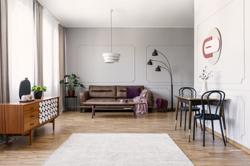 Black chairs at table near wooden cabinet in vintage living room interior with leather sofa. Real...