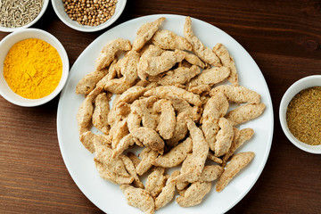 Raw dry soya meat chunks on a white plate on a wooden table with different species, top view