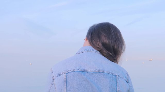 Woman in denim jacket sitting back listening to music and enjoying sea view