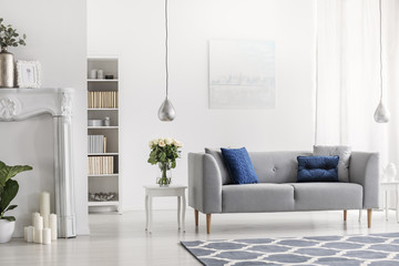 Grey settee with blue cushions in white elegant living room interior with flowers and painting. Real photo