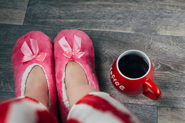 Feet in pink soft slippers and pajamas and red mug coffee near . Concept weekend.