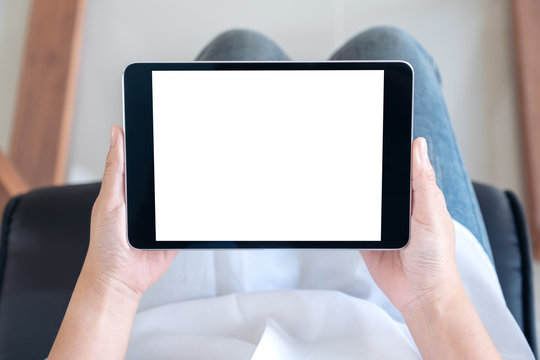 Top view mockup image of a woman holding black tablet pc with blank white screen while sitting on a chair