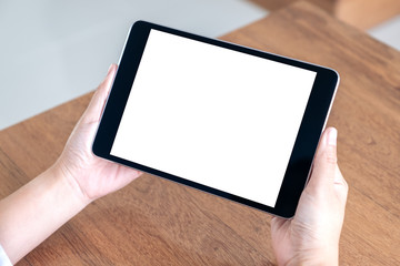 Mockup image of hands holding and using black tablet pc with blank white desktop screen while sitting in office