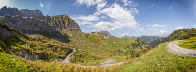 Panoramic view of the Col des Aravis in the French Alps. A dort road is going downhill toward the valley