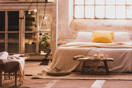 Cozy bedroom interior with a bed, stool, candles and industrial window. Real photo