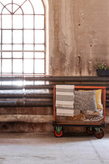 Trolley with pillows and blankets in a warehouse interior with an industrial window and radiator. Real photo