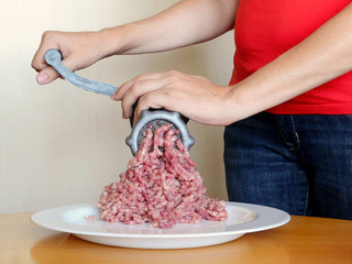Close up of women hands making mince with a vintage manual meat grinder on a beige background. Also it is white plate with mince on a wooden table