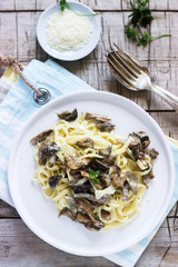 Tagliatelle with cream and forest mushrooms sauce in a white plate on a wooden background. Rustic style.