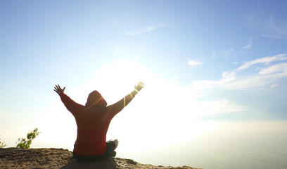 man sitting on mountain top viewpoint raised arm to the sky at sunrise