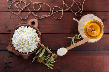 Obraz na płótnie Canvas Cottage cheese and cream. Soft cheese and honey on wooden boards. Cottage cheese in pottery and linden flowers. Twine on wooden background. Cream in wooden spoon. Honey on wooden stand. Copy space