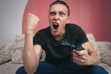 Aggressive gamer man with gamepad in the hand is playing in video game and is shaking his fist. Win a game concept. © Dmitriy