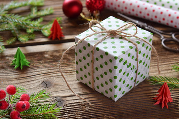 Fototapeta na wymiar Gift wrapping. Christmas composition with present box, packing paper, festive decoration and fir tree branch. Preparation for holiday. Merry Christmas and Happy New Year concept.