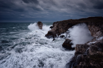 Obraz premium Dramatic nature background - big waves and dark rock in stormy sea, stormy weather. Dramatic scene. Contrasting colors.Beautiful natural landscape, seascape at Tyulenovo, Bulgaria. 