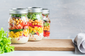 Fototapeta na wymiar Three glass jars with layering various vegan salads for healthy lunch. The concept of fitness and vegetarian food. Copy space.