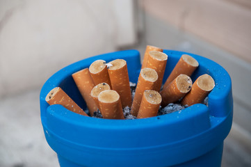 closeup of blue ashtray full of butt cigarettes