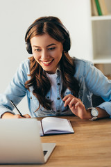 portrait of young smiling woman in headphones taking part in webinar in office