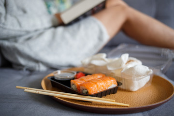 Young woman reading book and eating sushi