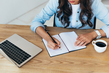 partial view of woman making notes while taking part in webinar in office