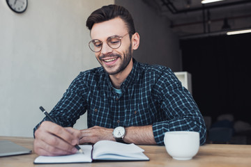 portrait of smiling businessman making notes in notebook at workplace in office