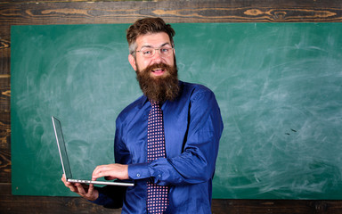 Teacher bearded man with modern laptop chalkboard background. Online education. Digital technology education. Modern technology education. Hipster teacher wear eyeglasses and necktie holds laptop