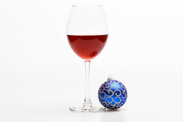 Winter celebration with alcohol drink. Glass with wine and christmas decoration. Wineglass with red liquid or wine and christmas ball ornament isolated on white background. Winter holidays concept