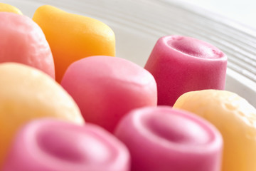 Close-up of pink and yellow colored soft sweet candy on a white plate against a white background