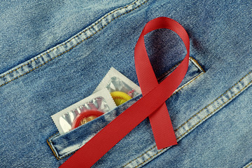 Colored condoms in a blue jeans pocket and Aids awareness red ribbon