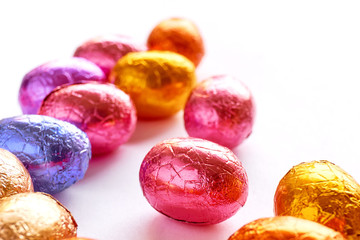 Many chocolate easter eggs wrapped in blue, purple, orange, pink and golden foil on a white background   