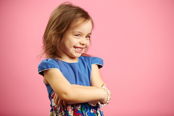 Children's beautiful girl with shyness stands on pink isolated background, wears fashionable dress...