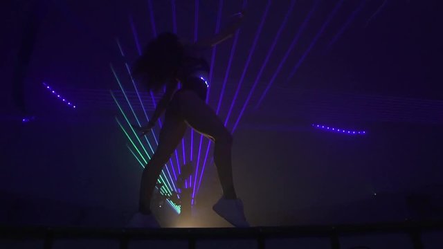 Fit girl doing gymnastics with lasers on the background, slow motion