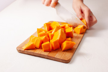 Cutting the pumpkin cubes on a white textured background