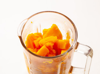 Chunks of cooked pumpkin in a blender on white background