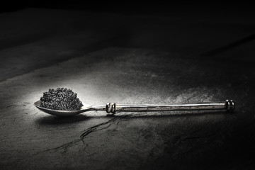 A photo of black caviar in a spoon, on a black background with copyspace - obrazy, fototapety, plakaty