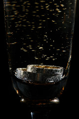 Wedding golden rings in glass of champagne. Symbol of love and marriage. Creative picture with champagne bubbles, glittering on black background