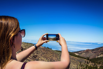 Young woman taking a photo with her phone of amazing mountains landscape on Tenerife, Canary islands, Spain. Travel concept