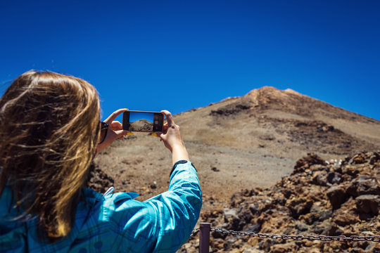 Young woman taking a photo with her phone of amazing mountains landscape on Tenerife, Canary islands, Spain. Travel concept