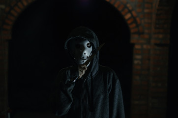 Fototapeta na wymiar man in a hood and hockey mask with a big knife on a black background