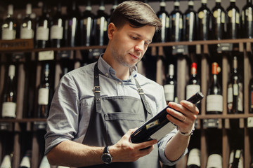 Young sommelier holding bottle of red wine in cellar