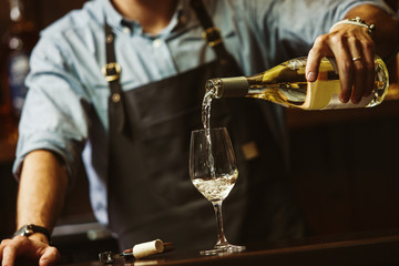 Male sommelier pouring white wine into long-stemmed wineglasses.
