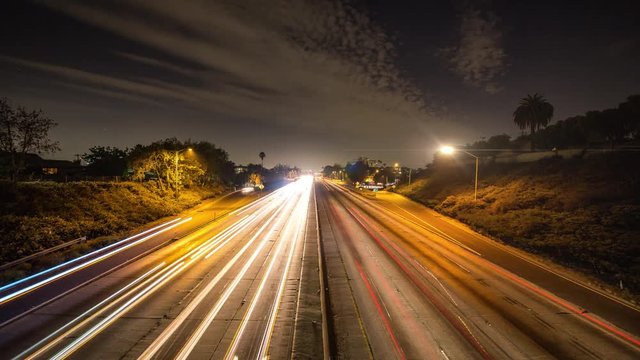 Time lapse of busy night traffic across freeway in Los Angeles. Blue sky with stars and scattered clouds.