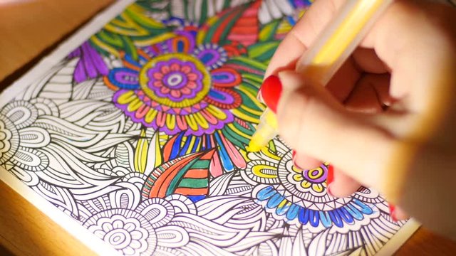 Painting adult coloring book at evening home by reading-lamp light