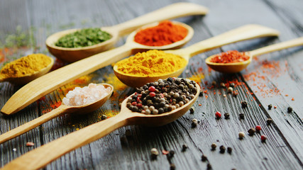 Closeup shot of nice wooden spoons with assorted dry spices lying on surface of dark lumber tabletop